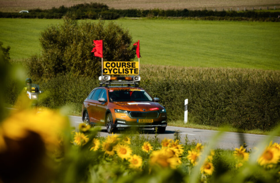 Voiture ouvreuse avec panneau "course cycliste" et drapeaux rouges